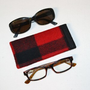 K&ouml;nnte beinhalten: Draufsicht mit zwei Brillen und einem rot-schwarz karierten Brillenetui. Eine Sonnenbrille hat dunkle Gl&auml;ser und einen dunklen Rahmen. Die andere Brille hat klare Gl&auml;ser und einen Schildpattrahmen.