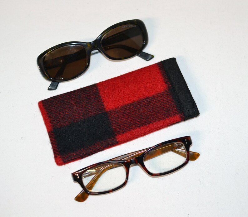 K&ouml;nnte beinhalten: Draufsicht mit zwei Brillen und einem rot-schwarz karierten Brillenetui. Eine Sonnenbrille hat dunkle Gl&auml;ser und einen dunklen Rahmen. Die andere Brille hat klare Gl&auml;ser und einen Schildpattrahmen.