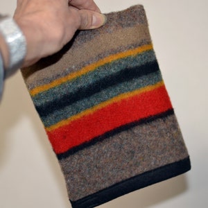 May include: A multi-colored striped wool blanket with a black border. The blanket is made of a thick, soft material and has a rustic look.