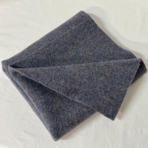 May include: A folded piece of dark gray fabric with a textured, heathered appearance. The material displays a dense, felted surface with subtle flecks of brown and blue fibers woven throughout the dark gray base, creating a uniform look.