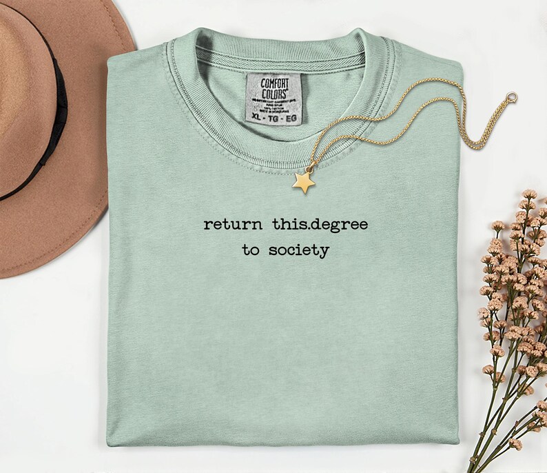 May include: A light green t-shirt with the text "return this.degree to society" in black. A gold necklace with a star pendant rests on the shirt. A brown hat is visible in the upper left corner.