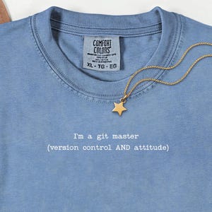 May include: A light blue Comfort Colors t-shirt with the text "I'm a git master (version control AND attitude)". A gold star pendant hangs from a gold chain. The shirt is size XL.
