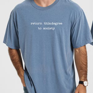 May include: A blue t-shirt with the text "return this.degree to society" in white. The shirt is a solid color and has short sleeves. The model is wearing a watch with a black band.