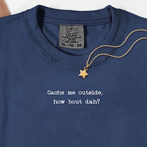 以下が含まれることがあります： 「Cache me outside, how bout dah?」の白文字がプリントされたネイビーブルーのTシャツ。ゴールドの星型ペンダントがゴールドチェーンから吊り下がっています。シャツにはComfort Colorsのタグ、サイズXL-TG-EGが付いています。
