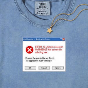 Può includere: Una t-shirt azzurra con etichetta Comfort Colors e una collana con stella dorata. La maglietta presenta la grafica di una finestra di errore del computer con il testo: adulting.exe - Application Error, ERROR: An unknown exception 0x4000015 has occured in adulting.exe. Reason: Responsibility not found. The application must terminate, con i pulsanti OK, Cancel e Ignore.