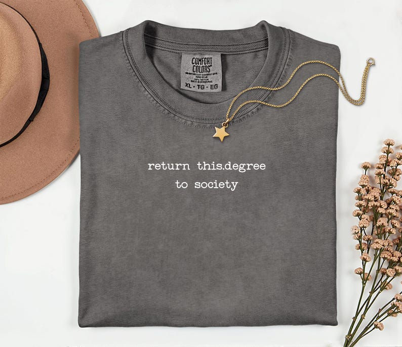 May include: A gray Comfort Colors t-shirt with the text "return this.degree to society" in white. A gold star pendant necklace and a brown hat are also in the image. The shirt is XL.