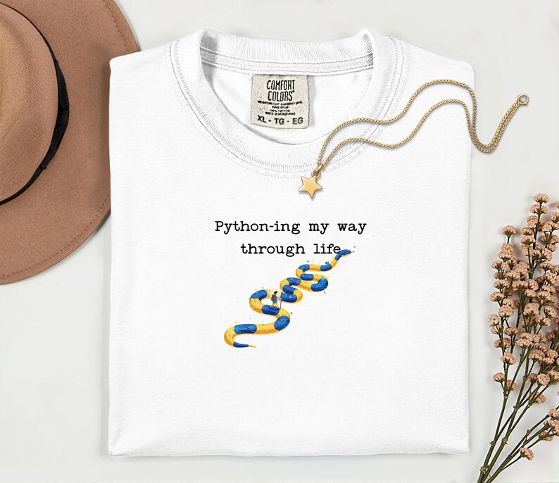 May include: White t-shirt with the text "Python-ing my way through life" and a blue and yellow snake graphic. A gold necklace with a star pendant is draped across the shirt.
