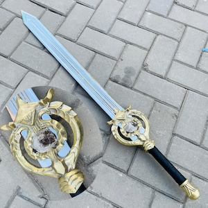 Puede incluir: Una espada decorativa con una hoja azul claro y una empuñadura dorada. La empuñadura presenta diseños intrincados y un mango negro. El diseño general de la espada sugiere un tema de fantasía o histórico.