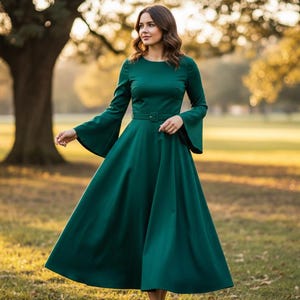 Pode incluir: Uma mulher vestindo um longo vestido verde esmeralda com mangas compridas e punhos largos. O vestido tem um corpete ajustado e uma saia fluida. A mulher est&aacute; em um parque com &aacute;rvores e luz solar ao fundo.