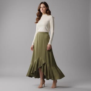 May include: A woman wearing a long-sleeved, off-white top and a flowing, olive-green skirt with a ruffled hem. The skirt falls to the ankles. She is wearing high heels. The background is a plain gray studio setting.