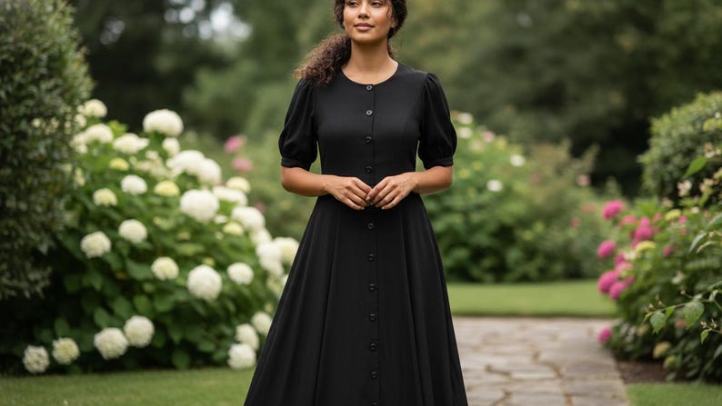 May include: A black dress with a button-down front and short, puffed sleeves. The dress has a fitted bodice and a flowing skirt. The woman is standing in a garden with white and pink flowers.
