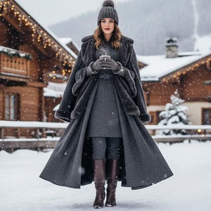 Pode incluir: Uma pessoa com um casaco de inverno cinzento, chap&eacute;u e luvas est&aacute; na neve, segurando uma ch&aacute;vena. O casaco tem uma saia longa e fluida e acabamento em pele. Botas castanhas e leggings escuros completam o traje. Edif&iacute;cios de madeira com luzes ao fundo.