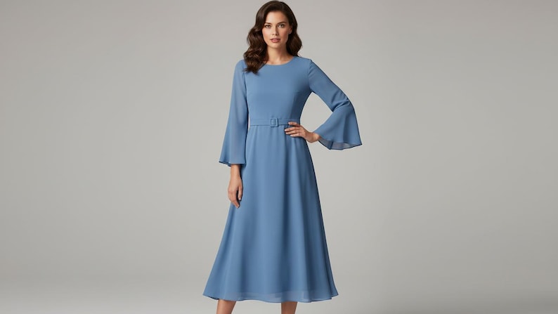 Pode incluir: Um vestido longo azul claro com mangas compridas e uma saia rodada. O vestido apresenta um pequeno cinto na cintura e mangas sino. A modelo est&aacute; vestindo o vestido em frente a um fundo cinza claro.
