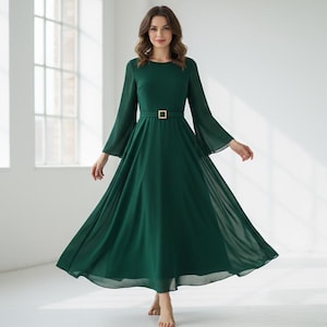 Pode incluir: Um vestido longo e esvoa&ccedil;ante verde esmeralda, com decote redondo e mangas compridas e largas. O vestido &eacute; cintado na cintura com um cinto retangular dourado. Feito de tecido leve, &eacute; adequado para eventos formais. O vestido tem cerca de 150 cm de comprimento.