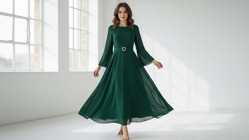 Pode incluir: Um vestido longo e esvoa&ccedil;ante verde esmeralda, com decote redondo e mangas compridas e largas. O vestido &eacute; cintado na cintura com um cinto retangular dourado. Feito de tecido leve, &eacute; adequado para eventos formais. O vestido tem cerca de 150 cm de comprimento.