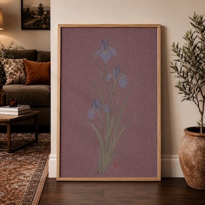 May include: A rectangular framed wall art piece featuring a botanical illustration of three blue iris flowers with green stems and leaves set against a solid, textured mauve background, enclosed within a light-toned wooden frame.