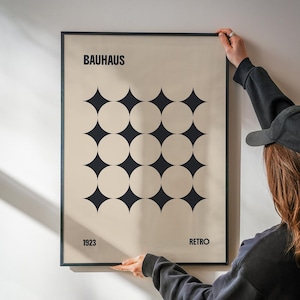 May include: A framed Bauhaus poster with a cream background and black geometric design. The poster features the word "BAUHAUS" at the top, the year "1923" at the bottom left, and the word "RETRO" at the bottom right. The design consists of a grid of alternating circles and diamond shapes.