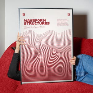May include: A framed poster with the title "WAVEFORM STRUCTURES" in maroon. The poster features a wavy pattern of maroon and white lines. The poster is held by a person wearing a black long sleeve shirt and blue jeans.