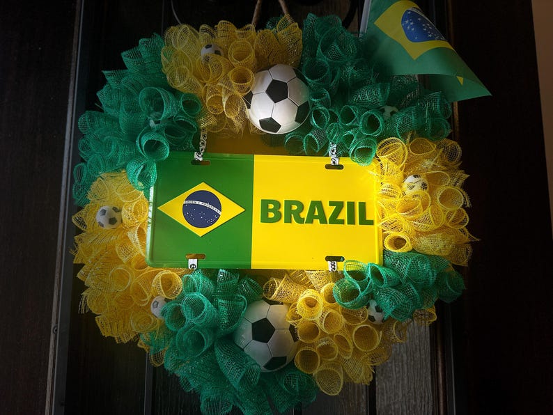 Puede incluir: Una corona decorativa con los colores de la bandera brasile&ntilde;a, con detalles en verde, amarillo y azul. La corona incluye un letrero que dice "BRAZIL" y una peque&ntilde;a bandera brasile&ntilde;a. Tambi&eacute;n se incorporan balones de f&uacute;tbol.
