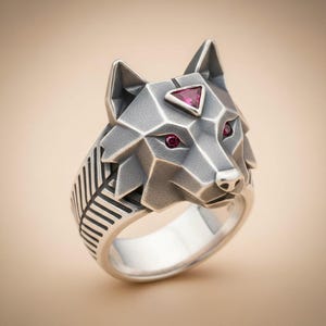 May include: A silver-colored ring featuring a geometric wolf head design. The wolf has red gemstone eyes and a triangular gemstone on its forehead. The ring band has a feather-like pattern. The ring is set against a neutral background.