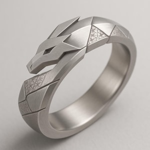 May include: A silver-colored ring with a geometric dragon design. The dragon's head is at the top, with detailed features and a textured pattern on the band. The ring has a modern, angular aesthetic.