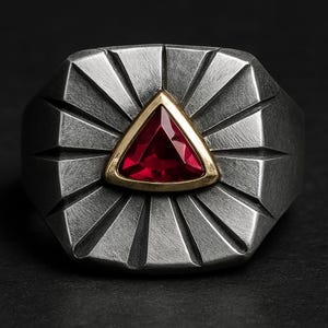 May include: A silver-toned ring with a geometric design. The ring features a triangular, deep red gemstone set in a gold-colored bezel. The ring's band has a textured, radial pattern emanating from the central stone.
