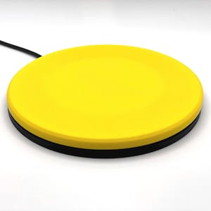 May include: A round, yellow foot switch with a black base and a black cable extending from the side. The switch is designed for hands-free operation and is likely used in various electronic devices.