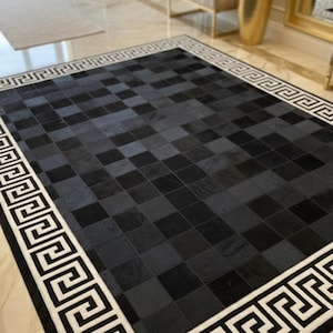 May include: A rectangular area rug with a checkered pattern in shades of black and gray. The rug has a white border with a repeating Greek key design. The rug is placed on a marble floor.