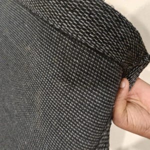K&ouml;nnte beinhalten: Nahaufnahme eines dunkelgrauen und wei&szlig;en gewebten Stoffes, m&ouml;glicherweise ein Textil oder Kleidungsst&uuml;ck. Der Stoff hat ein strukturiertes, gitterartiges Muster. Der Rand des Stoffes ist sichtbar und zeigt die Konstruktion des Gewebes.