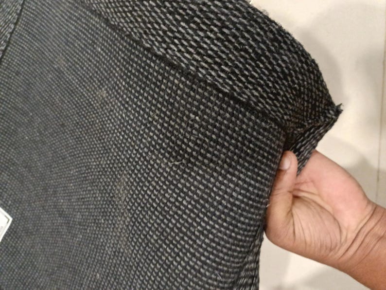 K&ouml;nnte beinhalten: Nahaufnahme eines dunkelgrauen und wei&szlig;en gewebten Stoffes, m&ouml;glicherweise ein Textil oder Kleidungsst&uuml;ck. Der Stoff hat ein strukturiertes, gitterartiges Muster. Der Rand des Stoffes ist sichtbar und zeigt die Konstruktion des Gewebes.