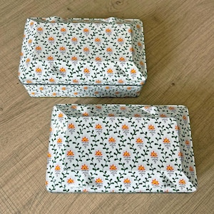 Puede incluir: Dos cajas rectangulares decorativas con tapas. Presentan un fondo blanco con un patrón repetido de vides verdes y diseños florales naranjas y amarillos. Ideales para almacenamiento o exhibición.