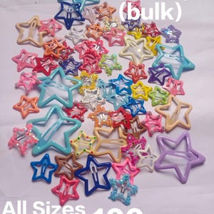May include: A collection of 100 star-shaped hair clips in various colours, including blue, pink, yellow, orange, and purple. Some clips feature glitter or small decorative accents. The image includes the text Star clips (bulk), All Sizes, and 100 pcs.