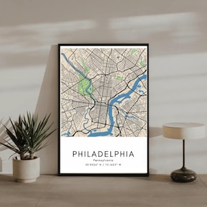 May include: A framed map print of Philadelphia, Pennsylvania, featuring a detailed street grid, blue rivers, and green park areas. The city name and coordinates are displayed in a white rectangular box at the bottom. The print is in a black frame.