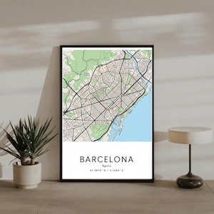 May include: A framed map print of Barcelona, Spain, featuring a detailed street layout in black and white, with green areas representing parks and a blue section for the coastline. The city name and coordinates are printed at the bottom.