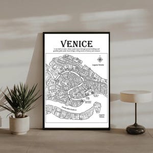 Puede incluir: Impresión enmarcada en negro de un mapa de Venecia, Italia. El mapa es una ilustración detallada en blanco y negro de los canales, puentes y edificios de la ciudad. El texto en la parte superior dice "VENICE". Se incluye una rosa de los vientos.