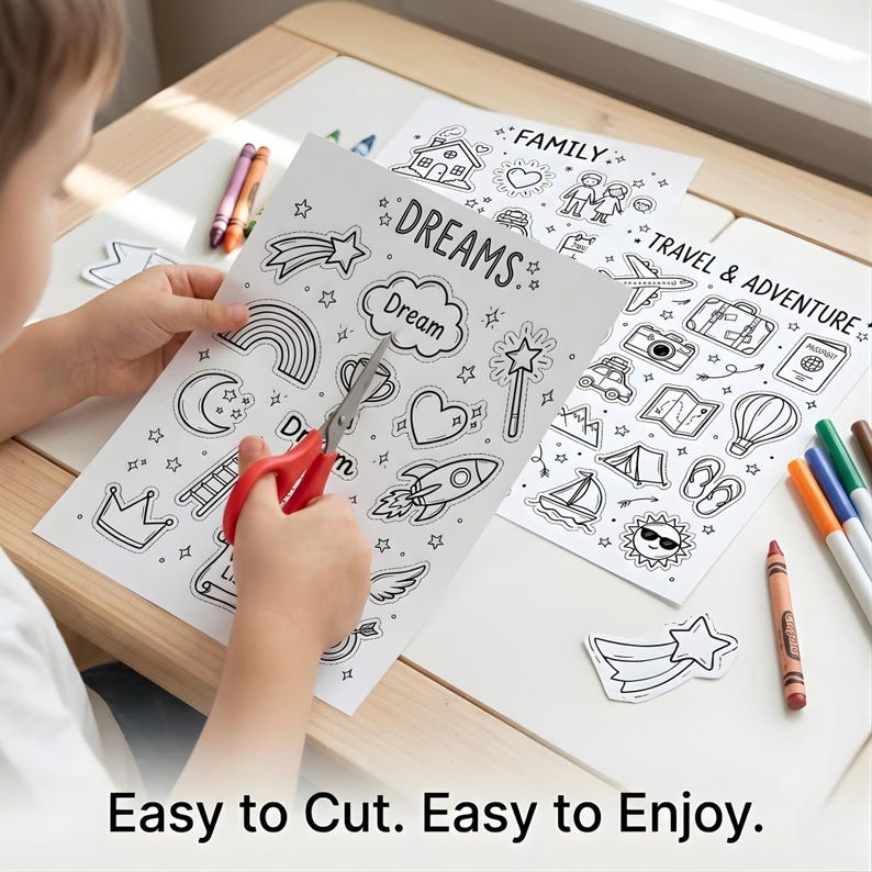 May include: A child uses red scissors to cut out a star from a black and white coloring sheet. The sheet is printed with the word "DREAMS" and various illustrations. Other sheets with illustrations and crayons are on the table. The text "Easy to Cut. Easy to Enjoy." is at the bottom.