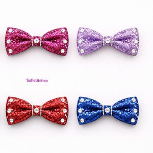 May include: Six glitter bow ties in gold, pink, purple, silver, red, and blue. Each bow tie is embellished with rhinestones and has a central rhinestone accent. The text "Sofistitchco" is in the center.