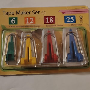May include: A Tape Maker Set in a clear plastic package. The set includes four different colored tape makers: green, yellow, red, and blue. The package has text that reads "Tape Maker Set" and includes the sizes 6, 12, 18, and 25.