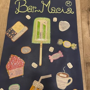 Può includere: Un poster blu scuro con la scritta "Bar Macia" in verde chiaro. Il poster presenta vari ritagli di carta di cibo e pillole, tra cui un ghiacciolo, un cupcake, una caramella e una tazza di caffè. Il testo "TACHIDOL" è visibile.