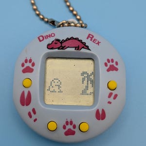 May include: A white ceramic mug with a black handle and the text "But First, Coffee" in a black, handwritten-style font. The mug is on a white surface. The mug is approximately 10 cm tall.