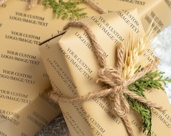 Puede incluir: Cajas de regalo envueltas en papel marrón, con el texto "YOUR CUSTOM LOGO/IMAGE/TEXT" impreso. Cada caja está atada con cuerda y adornada con ramitas verdes y espigas de trigo, creando una estética rústica y natural.