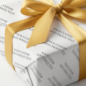 May include: A wrapped present with white paper printed with "YOUR CUSTOM LOGO/IMAGE/TEXT" in black. It is tied with a golden yellow satin ribbon, forming a bow on top. The overall presentation is clean and elegant.