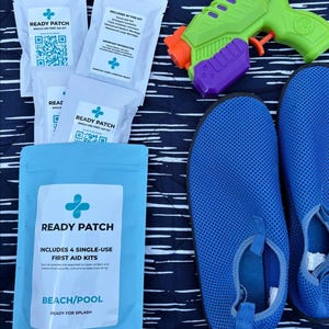 May include: A beach-themed collection featuring a blue first aid kit labeled "Ready Patch," containing single-use kits. Includes blue water shoes and a green and orange water gun. The items are arranged on a navy and white striped surface.