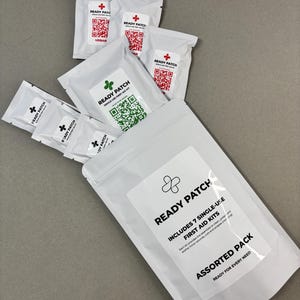May include: A white assorted pack of Ready Patch first aid kits. The pack includes 7 single-use kits with QR codes and the text "Ready Patch". The kits are designed for cleaning, protecting, and soothing minor wounds.