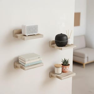 Puede incluir: Cuatro estantes flotantes de madera fijados a una pared blanca. Los estantes exhiben un altavoz blanco, un difusor de aceites esenciales negro, libros, una vela y una planta en maceta. Los estantes tienen un acabado de veta de madera clara.