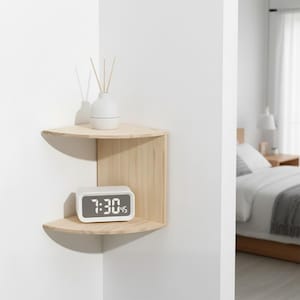 Könnte beinhalten: Ein helles Eckregal aus Holz mit zwei Ebenen. Das obere Regal enthält eine weiße Vase mit Schilf. Das untere Regal zeigt einen weißen digitalen Wecker mit der Uhrzeit 7:30 Uhr. Das Regal ist an einer weißen Wand montiert.