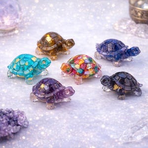 May include: A collection of seven decorative turtle figurines in various colors. The turtles have a mosaic-like design on their shells, with colors including blue, purple, brown, and multi-colored. The figurines are made of a translucent material.