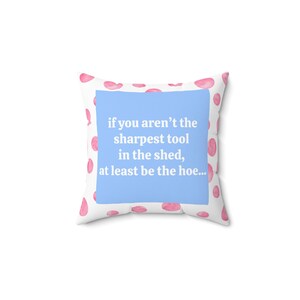 Può includere: Cuscino quadrato con sfondo bianco e pois rosa acquerello. Un quadrato azzurro al centro presenta il testo: "if you aren't the sharpest tool in the shed, at least be the hoe..."