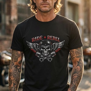 May include: A black short-sleeve t-shirt featuring a graphic of a skull wearing a helmet, flanked by two wings and crossed pistons. Above the skull, the text RIDE REBEL is printed in red with a small red star separating the two words.