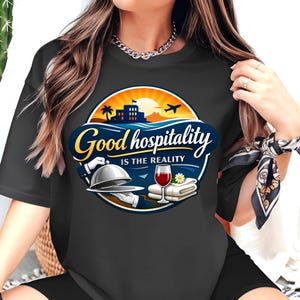 Puede incluir: Camiseta negra con un gráfico circular que dice "Good hospitality is the reality". El diseño incluye una puesta de sol, palmeras, un edificio y un avión. Debajo del texto hay imágenes de un camarero con una campana, una copa de vino y toallas dobladas.